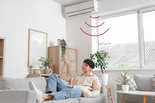 Junger Erwachsener liegt fr&ouml;hlich auf Sofa und bedient eine Klimaanlage per Fernbedienung