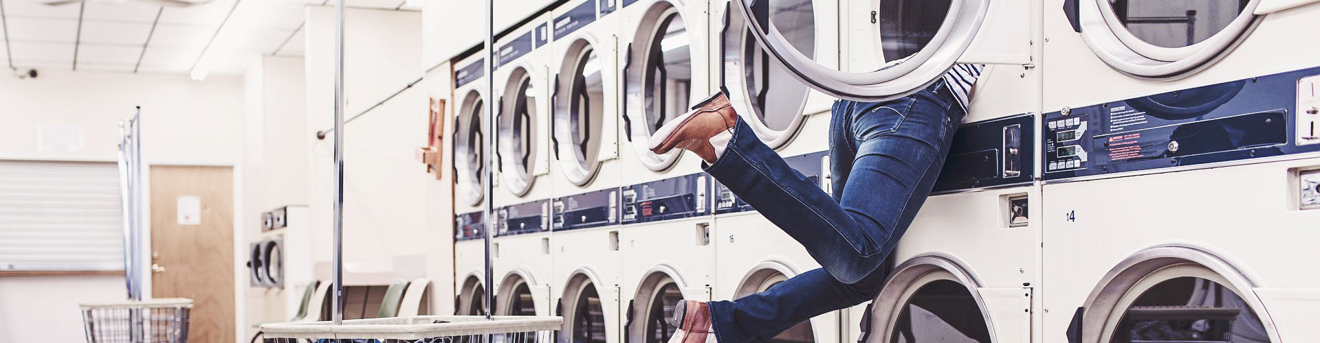 Eine Person steckt mit dem Oberk&ouml;rper in einer Waschmaschine eines Waschsalons fest