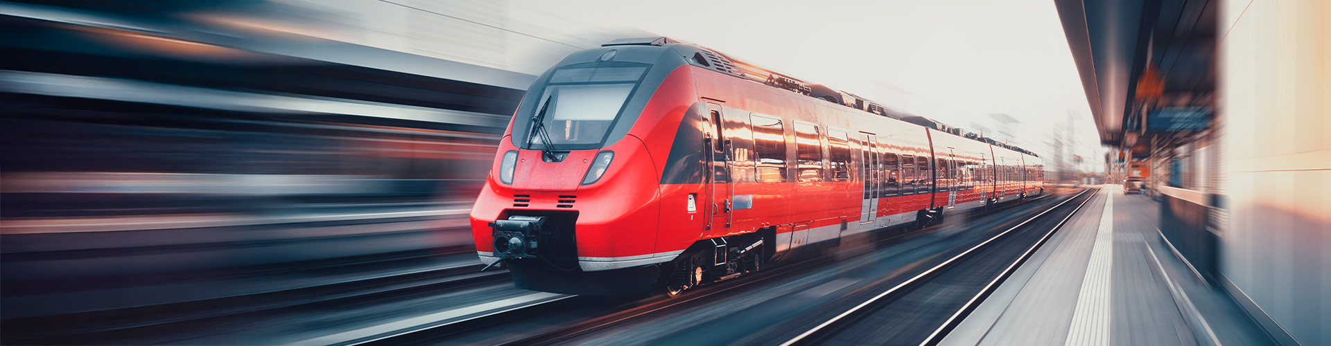 Ein roter Regionalzug f&auml;hrt durch einen Bahnhof