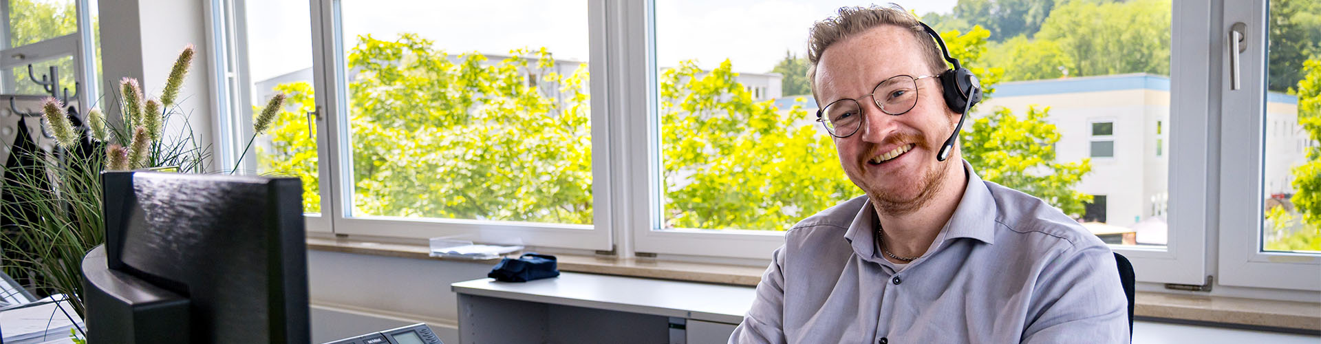 Mitarbeiter sitzt vor seinem Monitor am Schreibtisch und l&auml;chelt