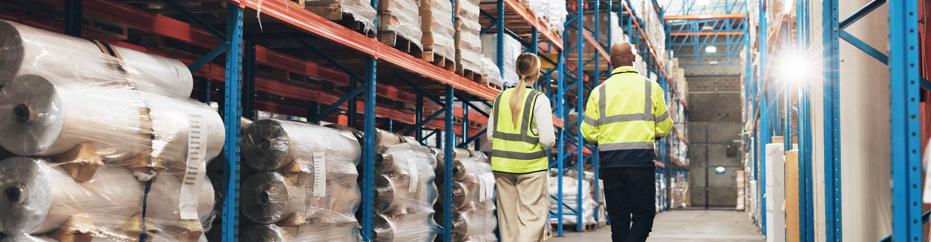Zwei Personen in Warnweste laufen zwischen Hochregallager und unterhalten sich
